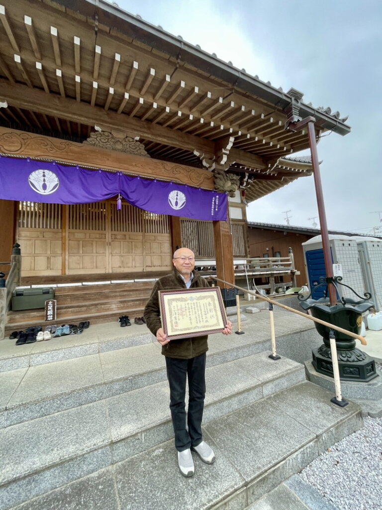 本堂前で賞状を持つ社長